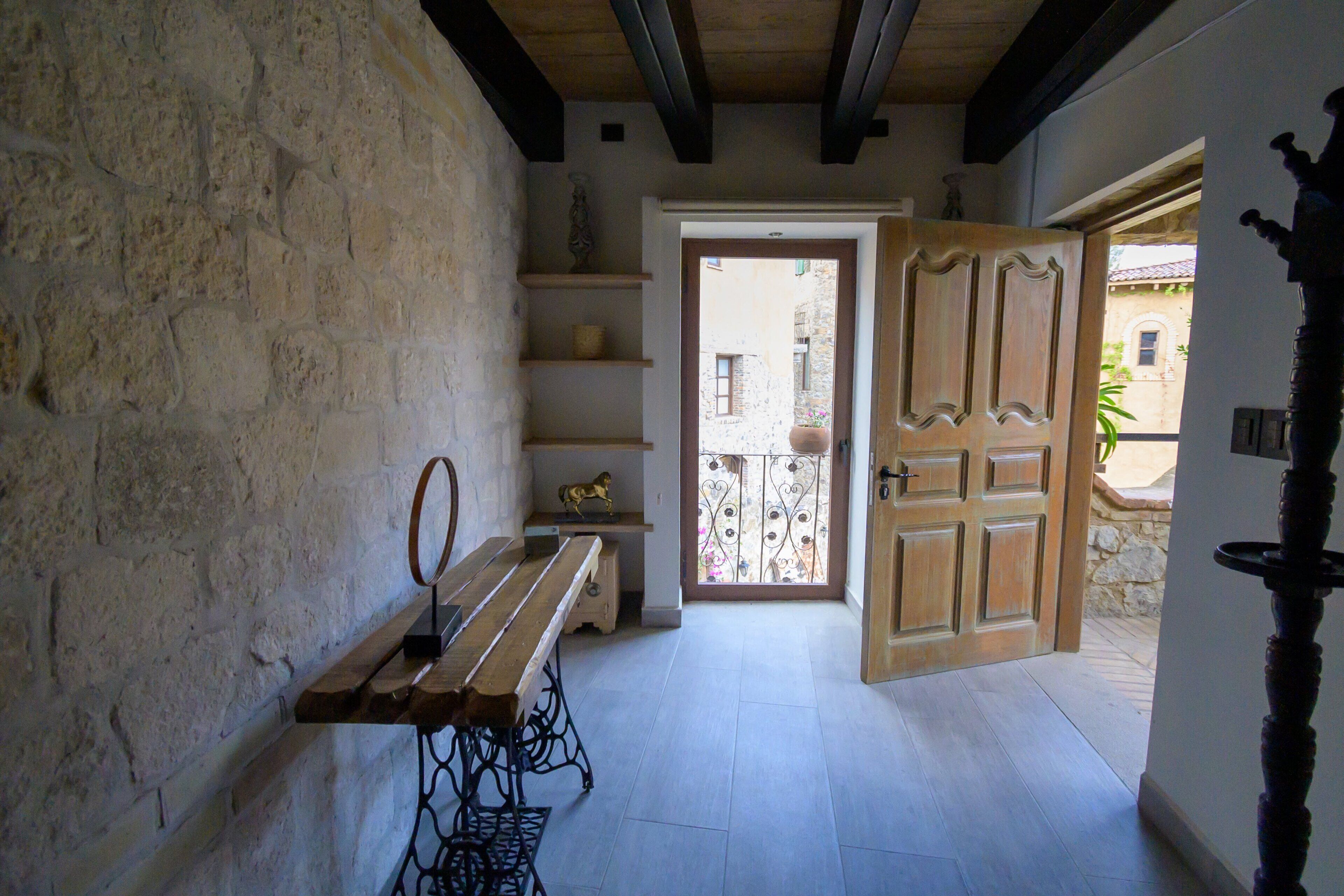 Un pasillo estrecho con un banco de madera, una máquina de coser y una puerta que da a un espacio exterior con balcón.