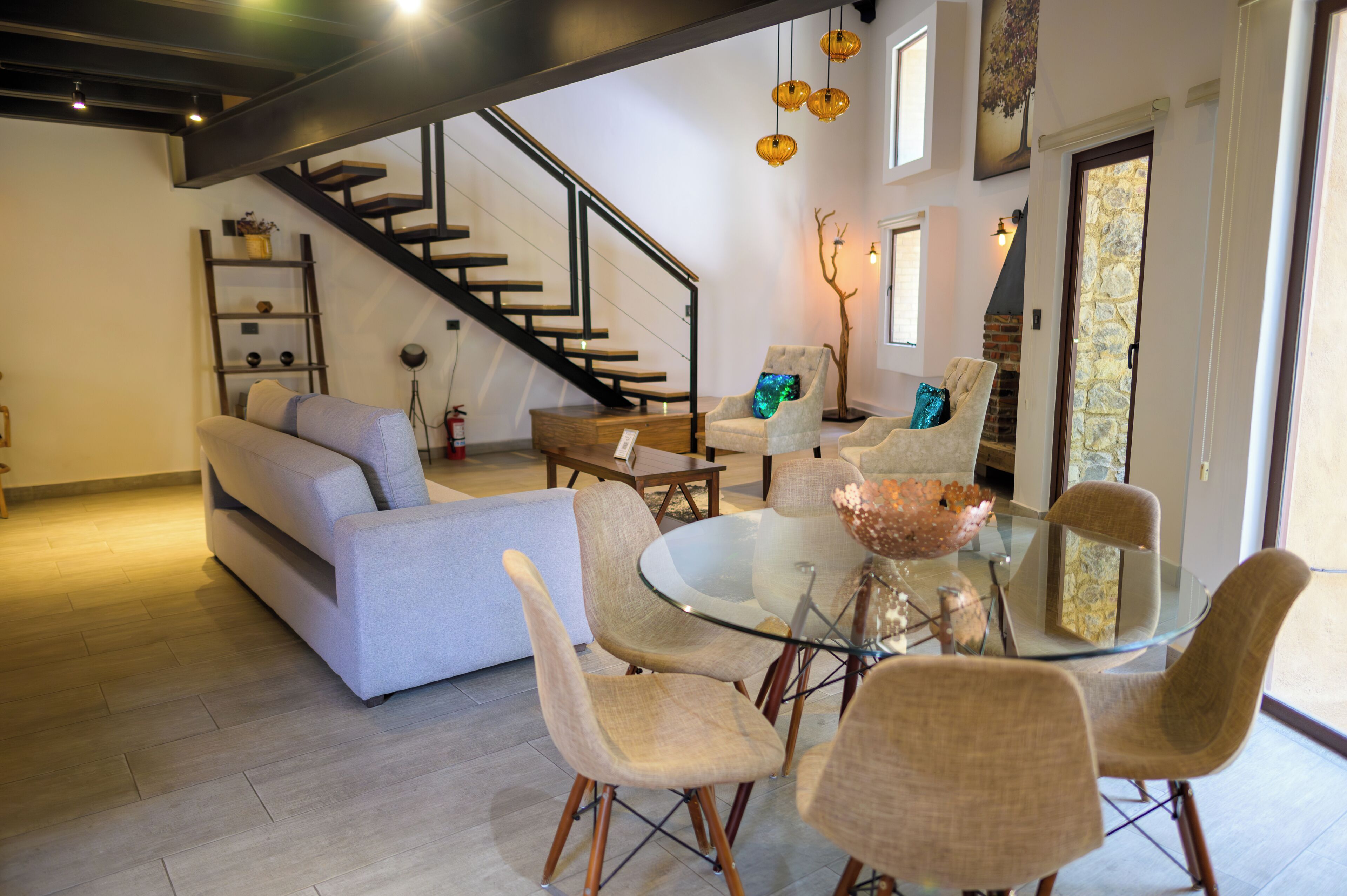 Una sala de estar moderna con un sofá, una mesa de comedor de cristal y sillas, una escalera y una pared de piedra.