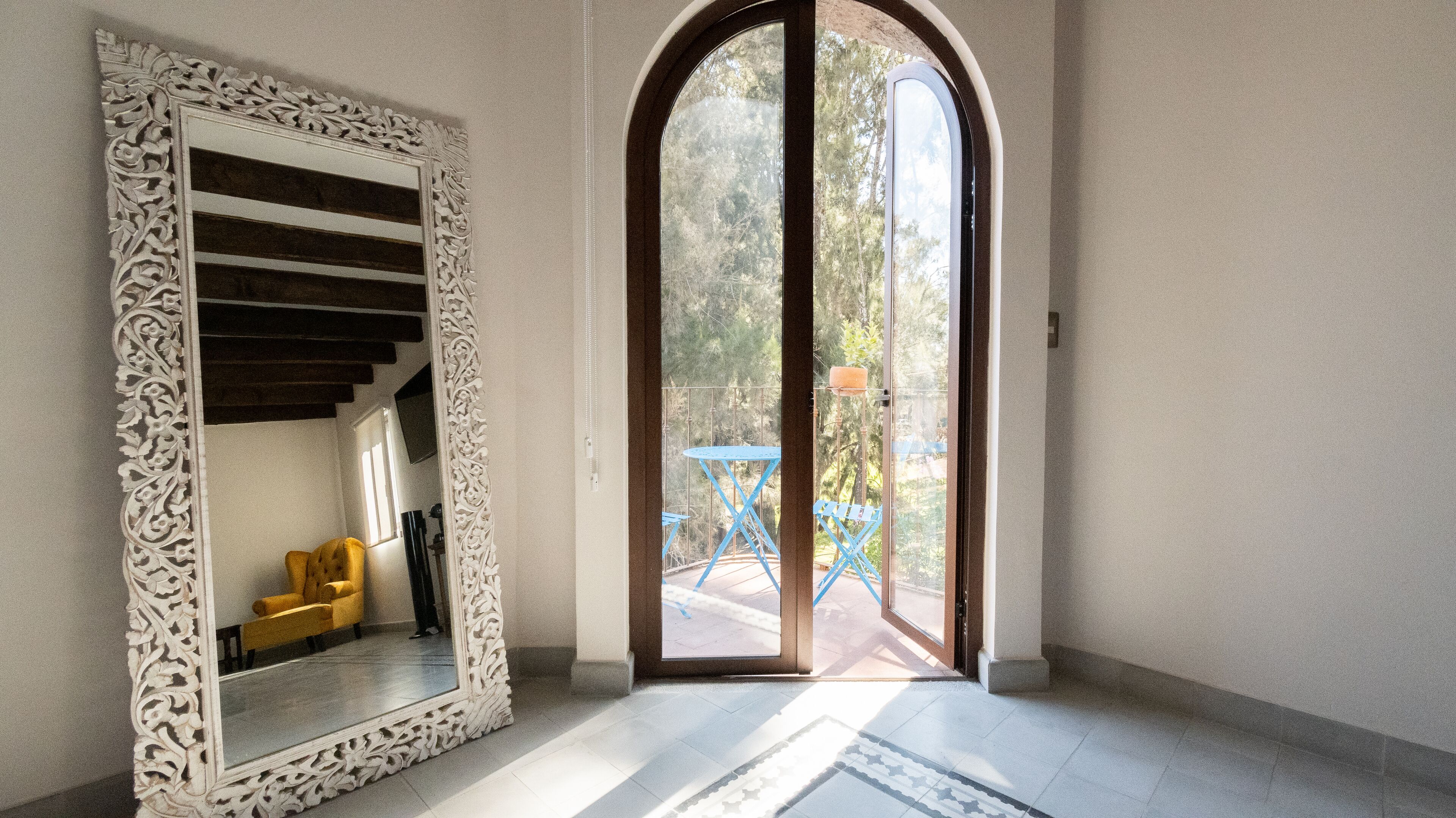 A room with a large ornate mirror, a wooden staircase, and a view of outdoor furniture through a glass door.