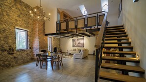A spacious living area with a stone wall, a dining table with chairs, a sofa, and a staircase with wooden steps.