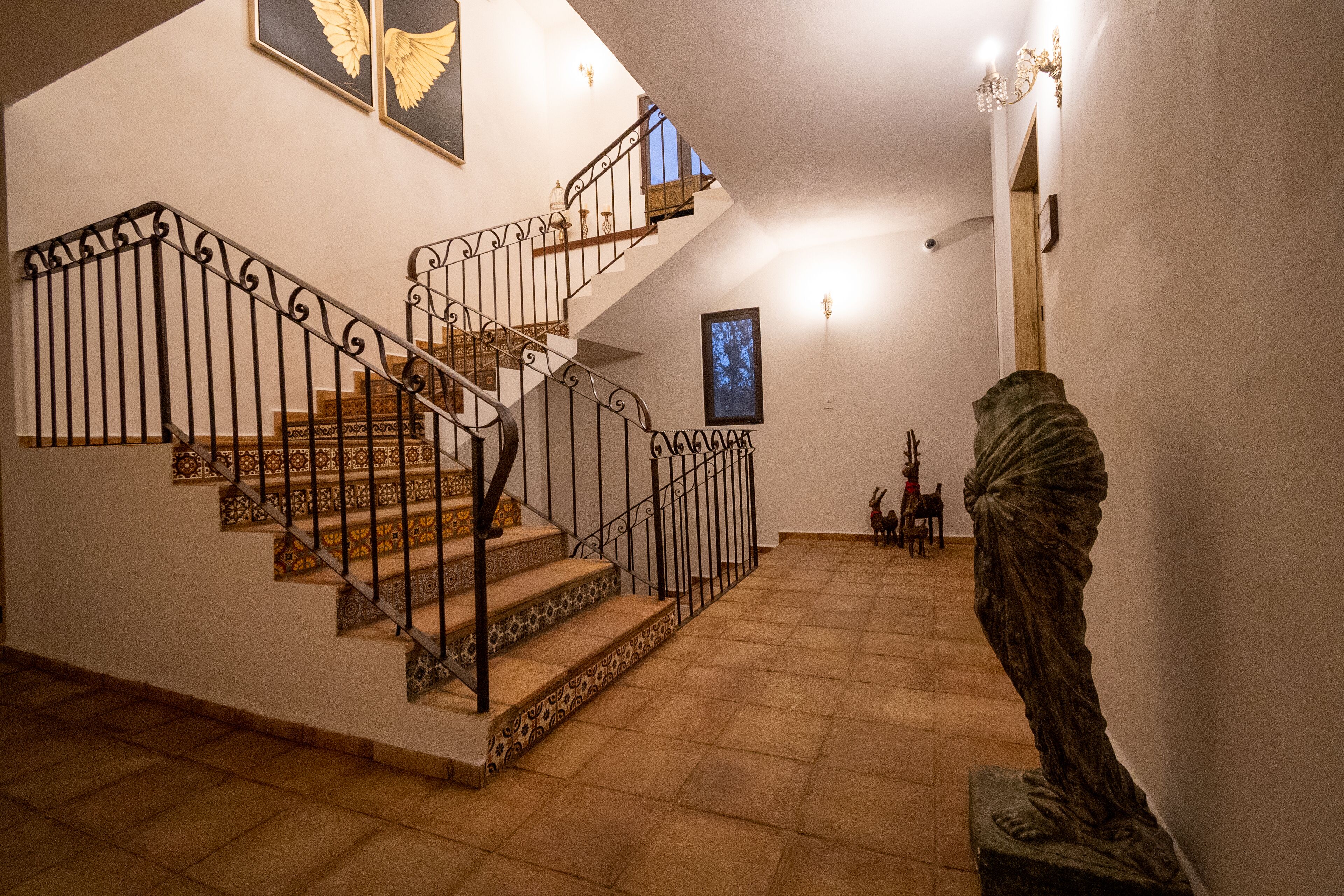 Una scala con ringhiere in metallo decorate, una statua e un quadro incorniciato al muro.