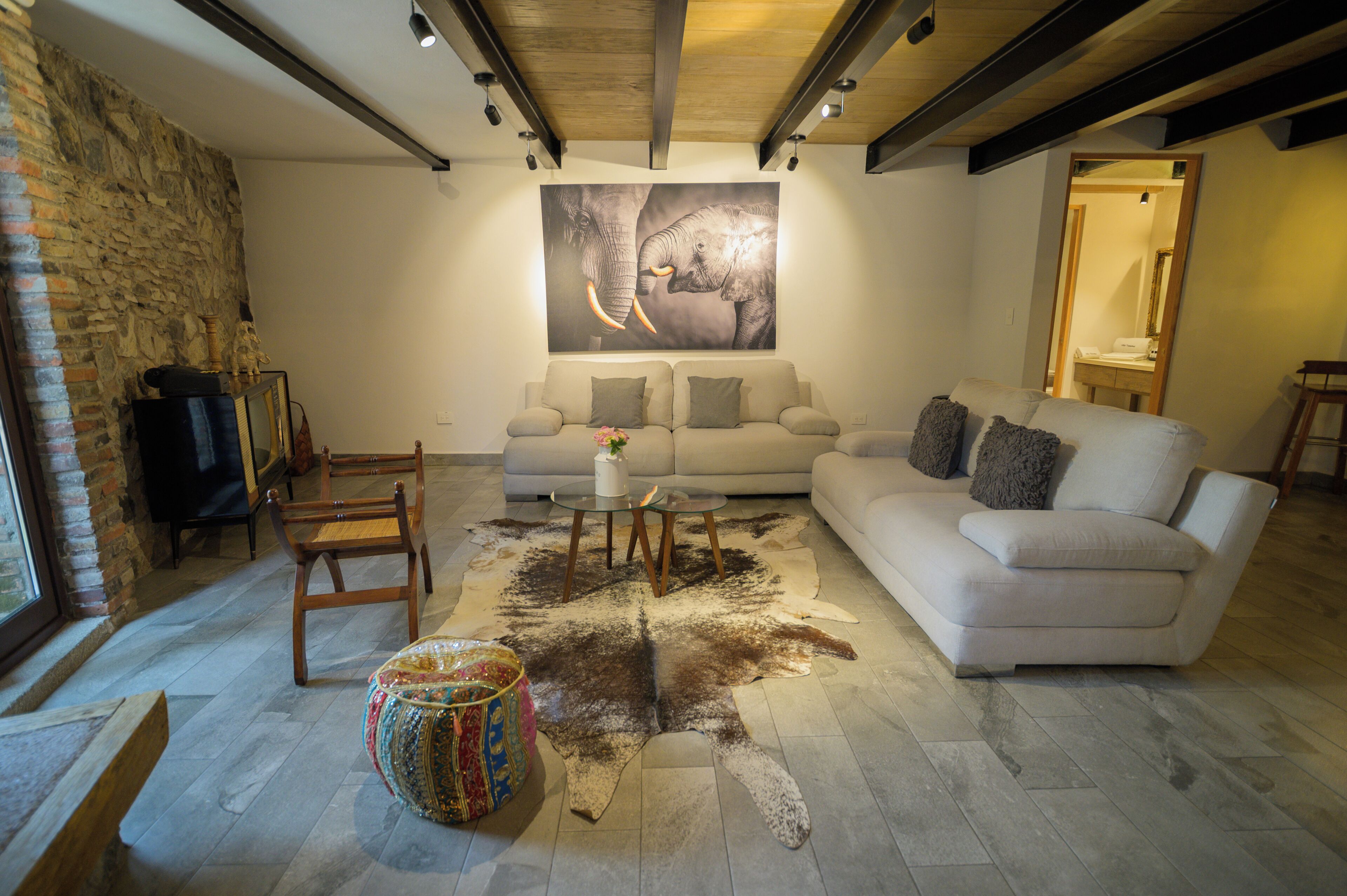 A living room with a stone wall, a white sofa, a glass coffee table, and a large elephant painting on the wall.