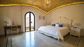 A bedroom with a large bed, a desk, and a chair. There is a door leading to an outdoor area.