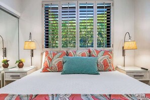 Une chambre à coucher avec un lit, deux tables de chevet, deux lampes et une fenêtre avec des volets.