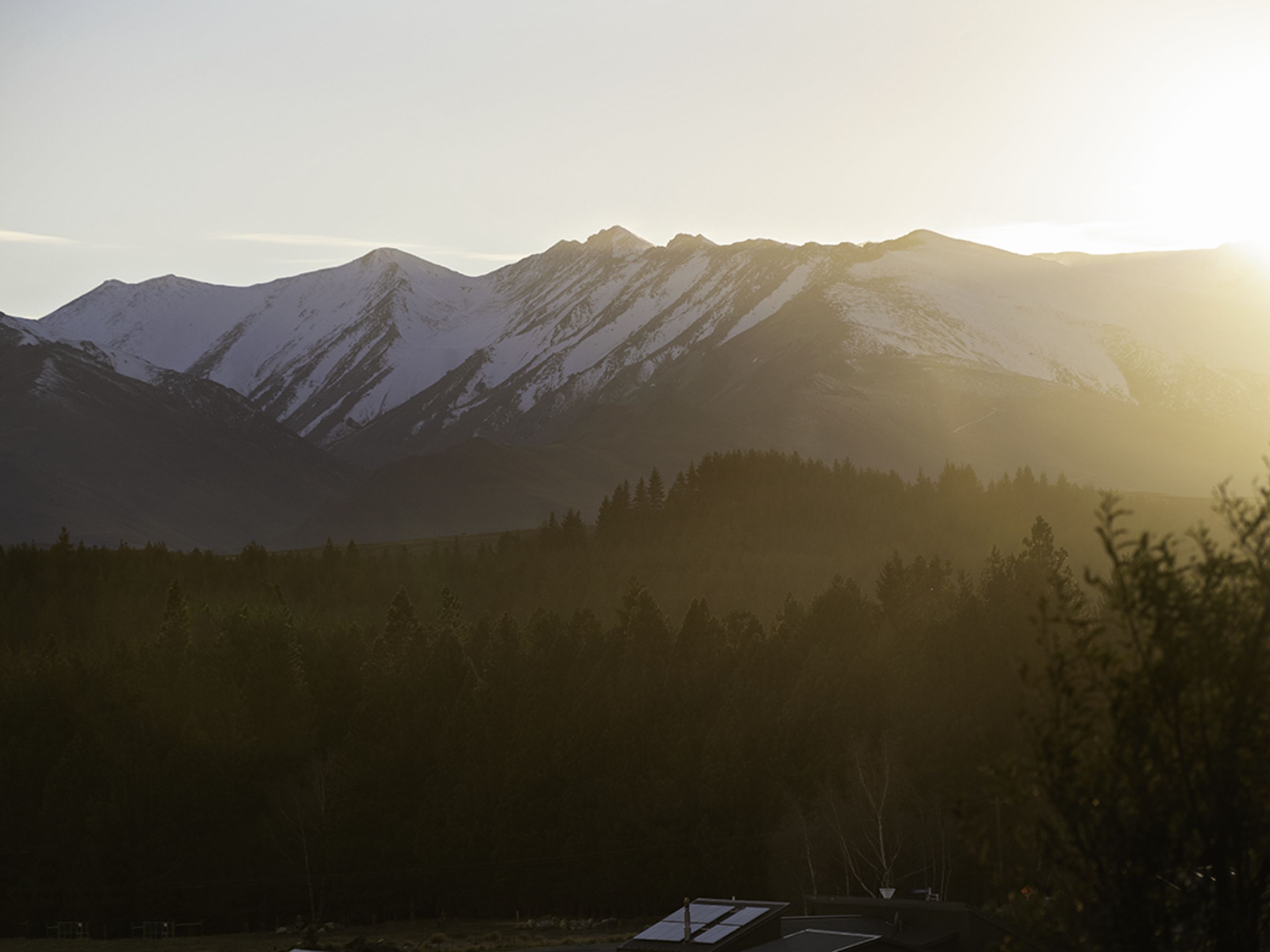 A mountain landscape with snow-capped peaks and a forested area in the foreground.