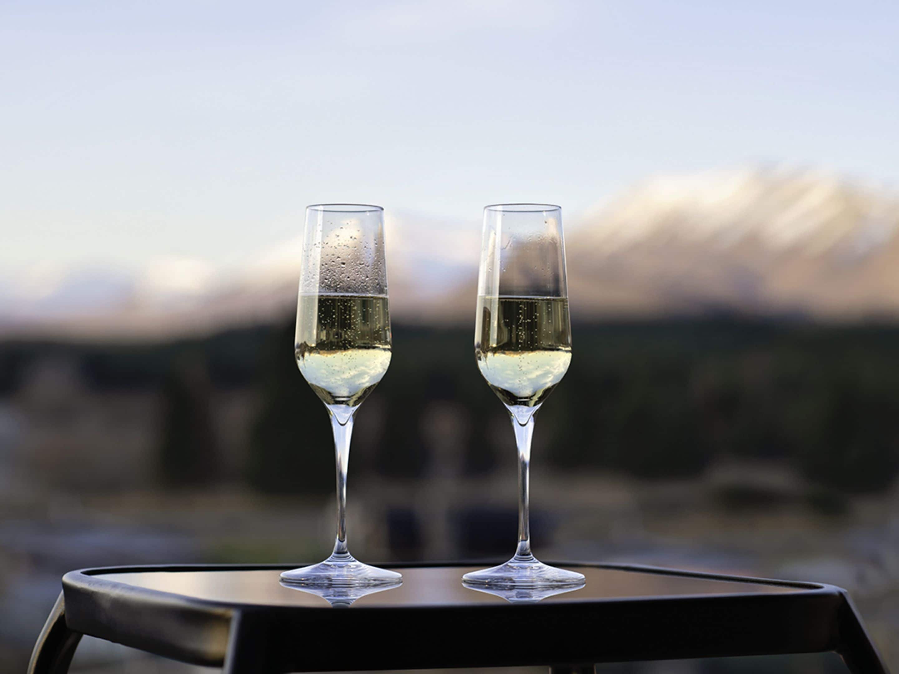 Dos copas de vino blanco sobre una mesa redonda con un fondo montañoso desenfocado.