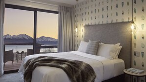 A hotel room with a large bed, a view of mountains through a balcony, and a table with chairs outside. - Ranginui at Lake Tekapo (Lake Tekapo)