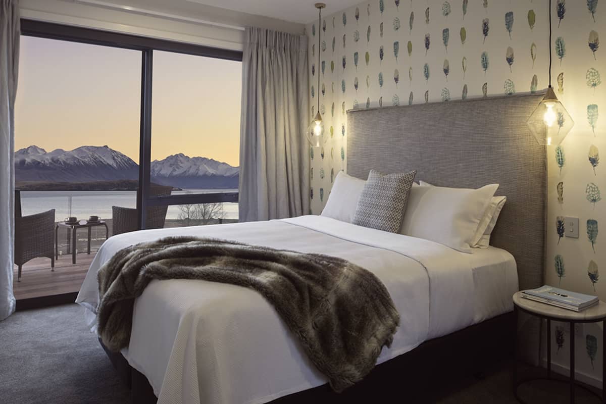 A hotel room with a large bed, a view of mountains through a balcony, and a table with chairs outside.