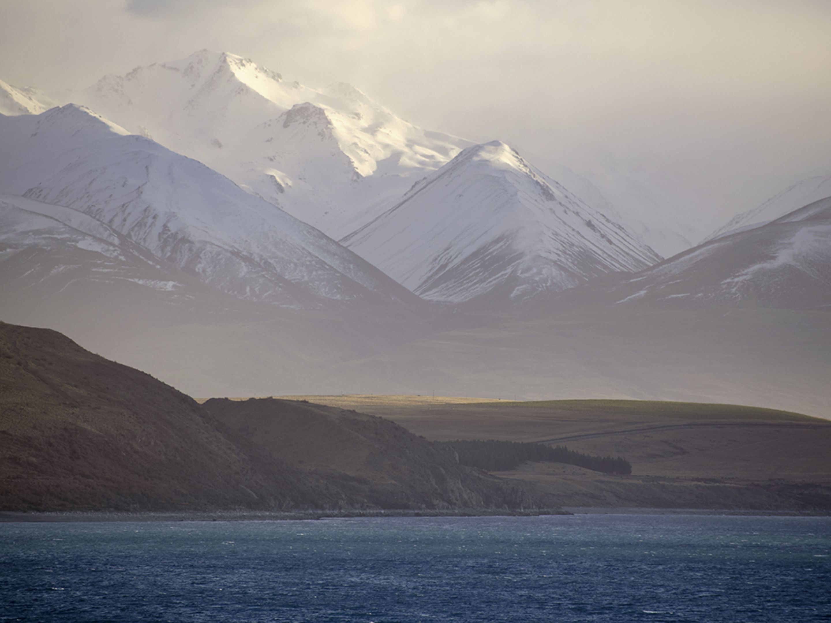 A mountainous landscape with snow-covered peaks and a body of water in the foreground.