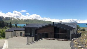 A modern building with a wooden facade and metal roof, situated by a body of water with mountains in the background. - Ranginui at Lake Tekapo (Lake Tekapo)