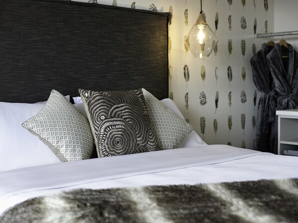 Una cama bien tendida con almohadas estampadas y un plaid de piel, una lámpara de noche y un armario con bata.