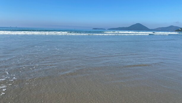 A beach with clear blue water and distant mountains.