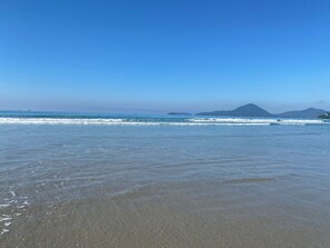 A beach with clear blue water and distant mountains.