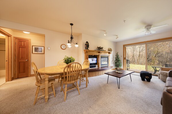A spacious living room with a large window, a dining area with wooden furniture, and a fireplace.