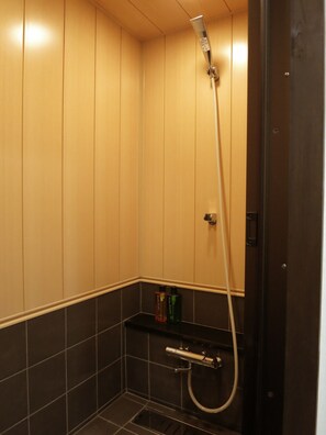 Shower area with a vertical showerhead and a small shelf for toiletries.