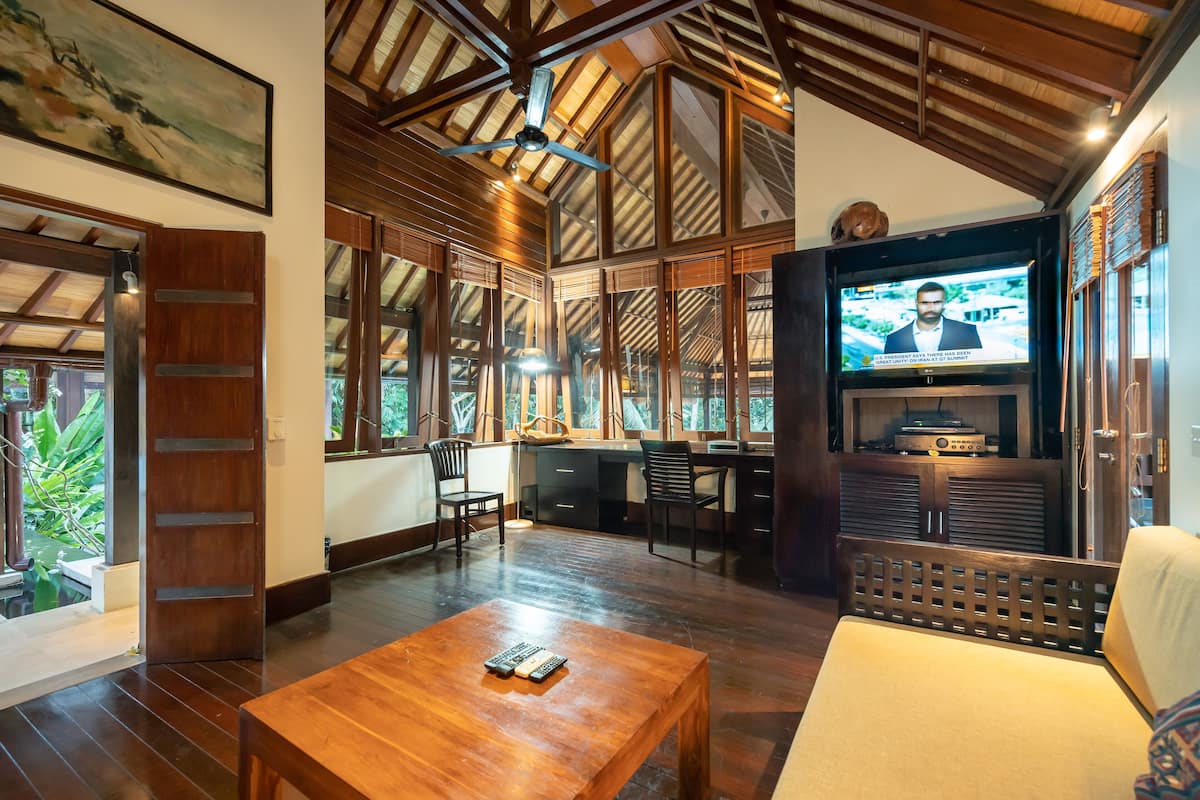 A spacious living area with a wooden ceiling, large windows, a television, and a dining table.