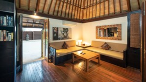 A cozy living room with a wooden ceiling, a sofa set, a coffee table, and a bookshelf. - Villa Vajra (Ubud)