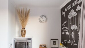 Une cuisine moderne avec des armoires blanches, un four à micro-ondes, un réfrigérateur et un évier. Il y a une horloge au mur et un élément décoratif fixé au mur au-dessus de l’évier.
