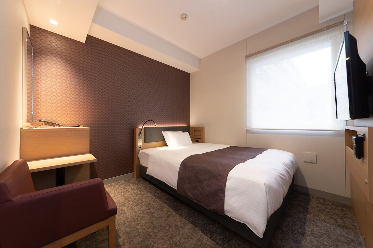 Una habitación de hotel con cama, escritorio, silla, televisor y ventana.