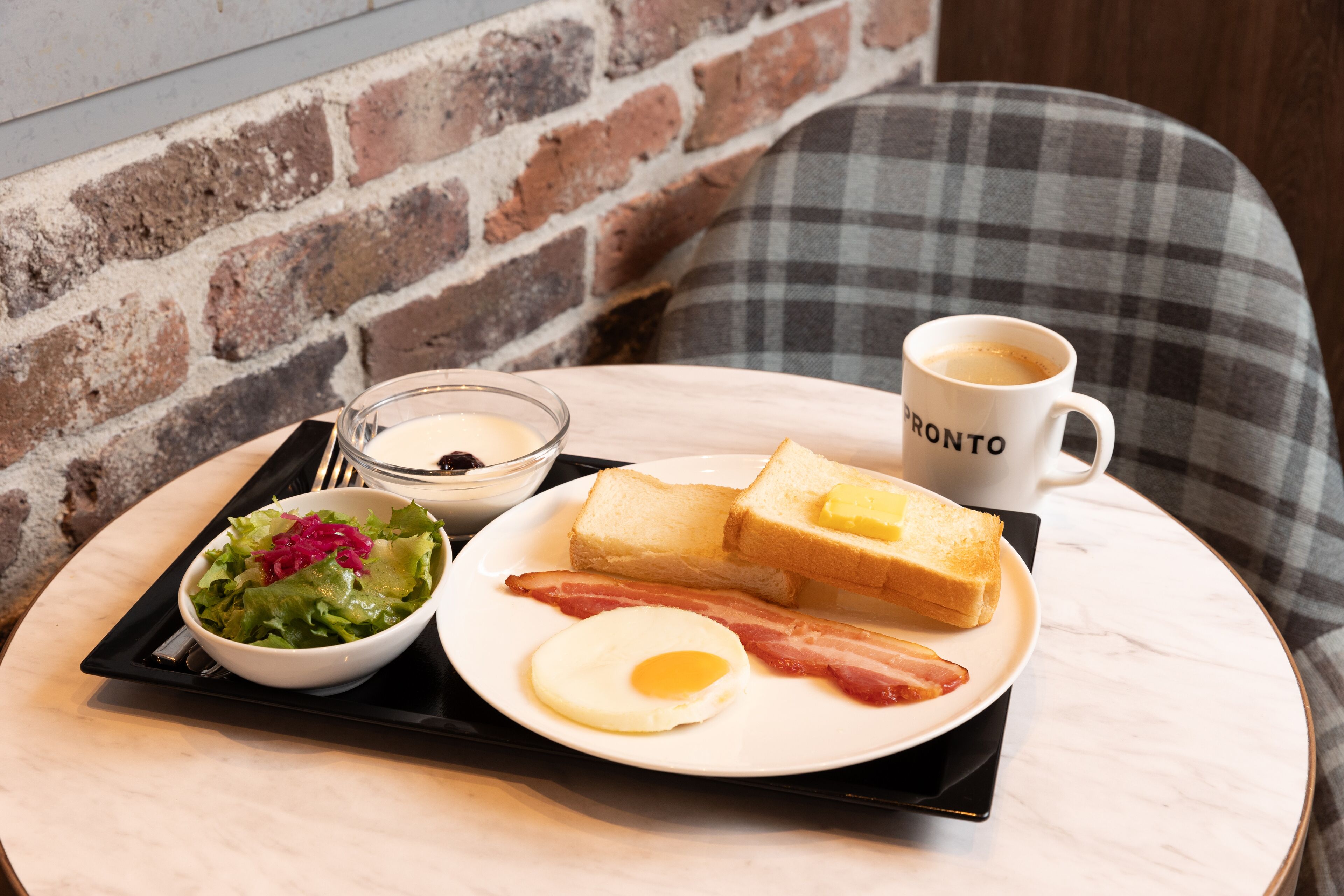 A breakfast tray with toast, bacon, an egg, a bowl of salad, and a cup of coffee on a round table.