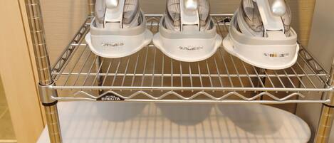 A kitchen with three white electric kettles on a metal shelf, a white plate below, and a wall with a wooden panel.