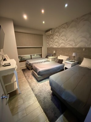 Habitación de hotel con dos camas, un escritorio, una silla, una mesita de noche con lámpara y aire acondicionado instalado en la pared.