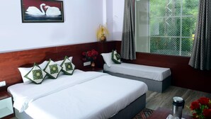 A hotel room with two beds, a wooden headboard, a framed picture of swans, a window with curtains, and a vase with red flowers. - Meera Mahal (Sawai Madhopur)