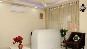 A reception area with a white reception desk, a brown leather chair, a potted plant, and a clock on the wall. - Meera Mahal (Sawai Madhopur)