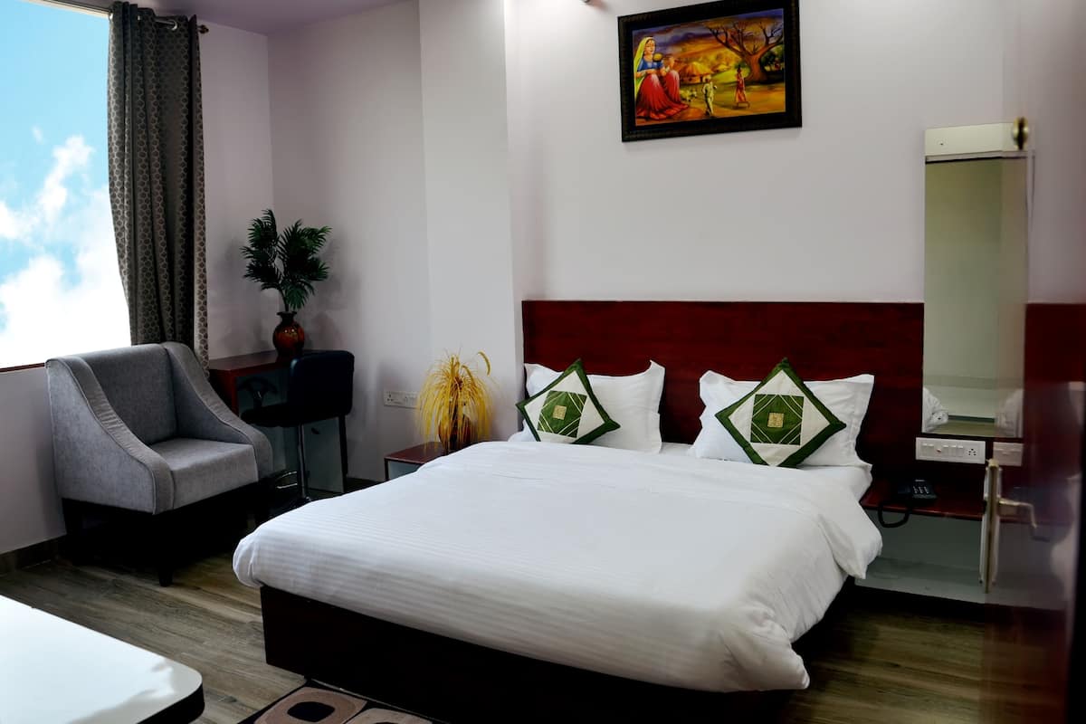 Ein Hotelzimmer mit einem großen Bett, einem Sessel, einem Schreibtisch, einer Pflanze und einem Bild an der Wand.