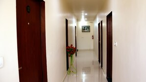 A hotel hallway with wooden doors, a framed picture on the wall, and a vase with red flowers on the floor. - Meera Mahal (Sawai Madhopur)