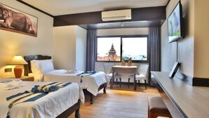 A hotel room with two beds, a dining table, a TV, and a view of a temple. - Tapae Place Hotel (Chiang Mai)