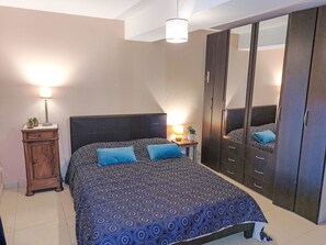 Une chambre à coucher avec une couvre-lit à motifs, une armoire en bois, une table de chevet avec une lampe et un miroir sur la porte de l’armoire.