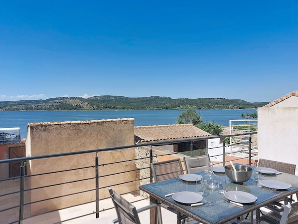 A terrace with a table set for dining, overlooking a body of water and hills.
