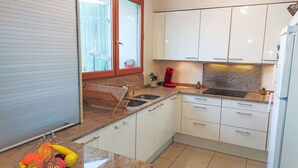 A kitchen with white cabinets, a stainless steel sink, a red kettle, and a fruit basket on the counter. - La Maison de l'Etang by Interhome (Gruissan)