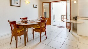 A dining area with a round table and chairs, a kitchen area with a counter, and a sliding glass door leading to a balcony. - La Maison de l'Etang by Interhome (Gruissan)