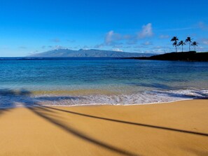 A beach with clear blue water, a sandy shore, and a mountain in the background. - OCEAN FRONT, ground level, end unit. (kihei)