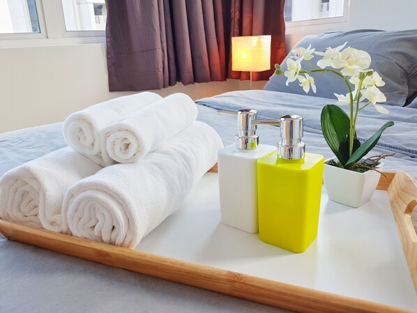 A neatly made bed with white towels, a bedside table with toiletries, and a potted orchid.