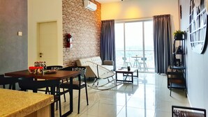A modern living room with a dining area, a brick accent wall, a ceiling fan, and a large window with curtains. - Teiw Family Homestay at Skypod Residence Puchong (Puchong)