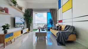 A modern living room with a flat-screen TV, a sofa, a coffee table, and a balcony with a view.
