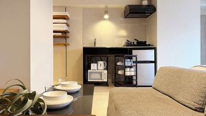 A compact living space with a kitchenette, a sofa, and a dining table with bowls and plates. - ORIGAMINN 601 by b hotel - 5 mins PeacePark (Hiroshima City)