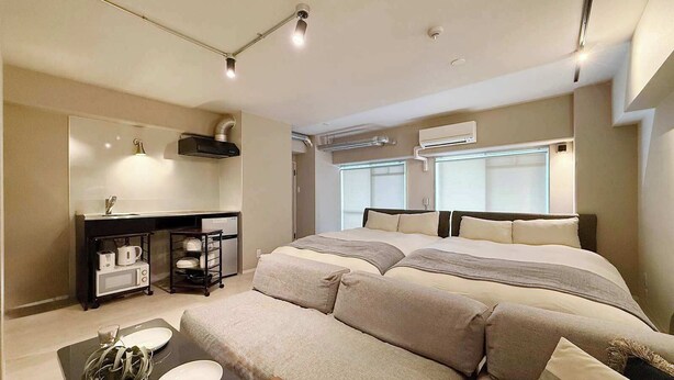 Ein modernes Hotelzimmer mit einem großen Bett, einer kleinen Küchenzeile und einer Sitzecke mit Tisch und Stühlen.