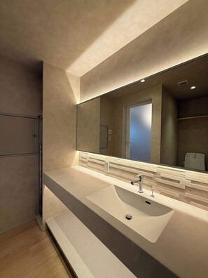 A modern bathroom with a large mirror, a white sink, and a tiled backsplash. - Newly Renovated 3BR｜Island Kitchen｜Station 1 min (Hiroshima City)
