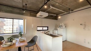 A modern kitchen with a central island, a dining area with a table and chairs, and a view of the city through a large window.