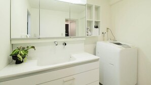 A bathroom with a white sink, a mirror, a white washing machine, and a small shelf with toiletries.