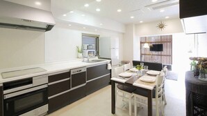 A modern kitchen with built-in appliances, a dining area with a table set for four, and a TV mounted on the wall.