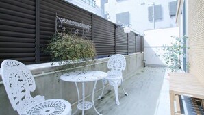 A balcony with white metal chairs and tables, a small wooden bench, and a potted plant.