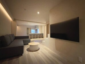 Un salon moderne avec un grand téléviseur à écran plat fixé au mur, un canapé de couleur foncée et une table basse ronde.