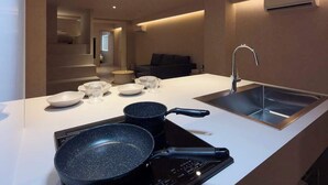 A modern kitchen with a white countertop, a black induction cooktop, a sink, and a built-in range hood. - Renovated Double Bunk Bed & 2-Bath｜near Peace Park (Hiroshima City)