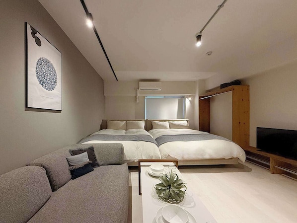 A modern bedroom with a bed, a sofa, a TV, and a wall-mounted air conditioner.