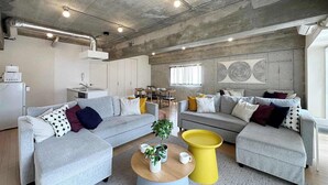 Un salon moderne avec un canapé gris, une table basse jaune et un coin cuisine à l’arrière-plan.